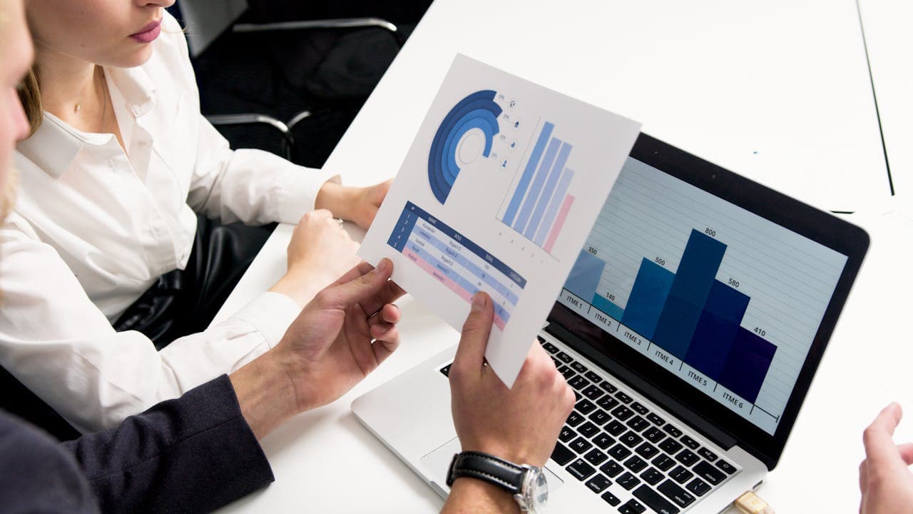 People holding printed charts and computer showing graphs